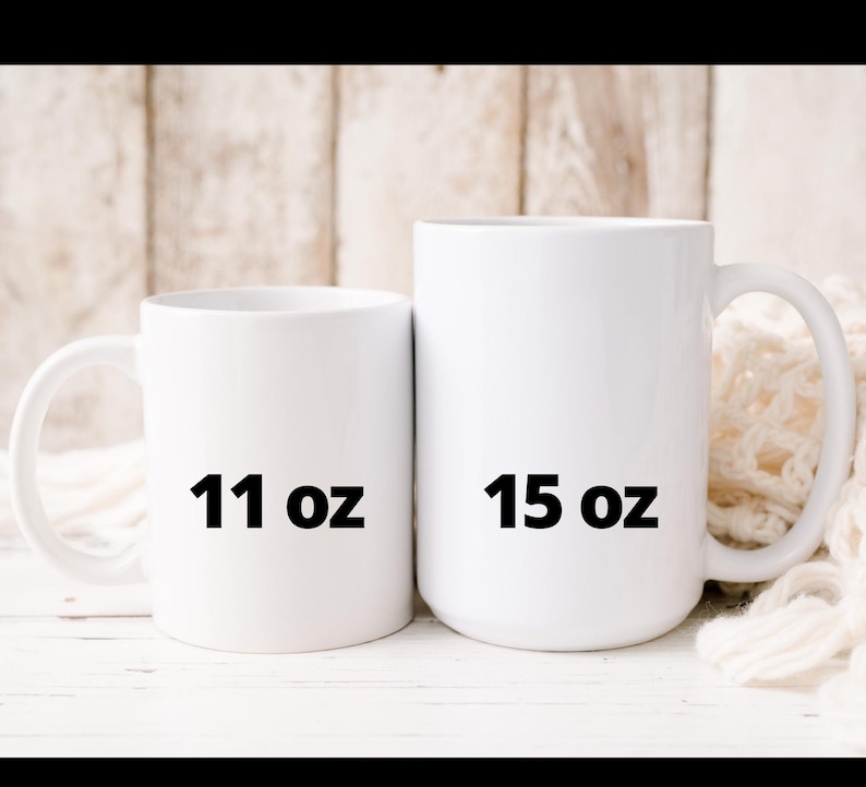 May include: Two white ceramic mugs, one labeled "11 oz" and the other "15 oz". The mugs have a simple, clean design with a curved handle. The background is a light wooden surface.