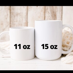 May include: Two white ceramic mugs, one labeled "11 oz" and the other "15 oz". The mugs are displayed against a light-colored wooden background with a soft, white fabric in the background.