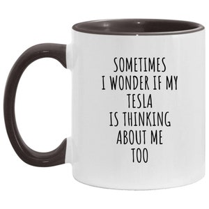 May include: White ceramic coffee mug with a black interior and handle. The mug has black text that reads "Sometimes I wonder if my Tesla is thinking about me too."