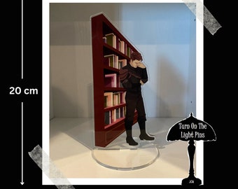 Könnte beinhalten: Ein klarer Acrylständer mit einer Figur in schwarzer Kleidung vor einem roten Bücherregal. Der Ständer ist 20 cm hoch und 9,6 cm breit. Der Text "Turn On The Light Pins" ist sichtbar.