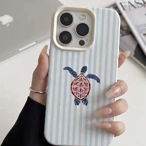 Peut inclure: Coque de téléphone à rayures bleues et blanches avec un motif de tortue. La tortue a une carapace rouge et bleue et des nageoires bleues. L'étui a un bord blanc autour de l'appareil photo.