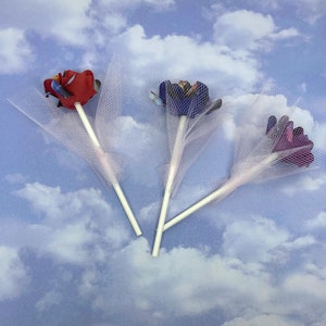 Puede incluir: Tres ramos de flores de papel con tul blanco. Las flores son rojas, moradas y azules.