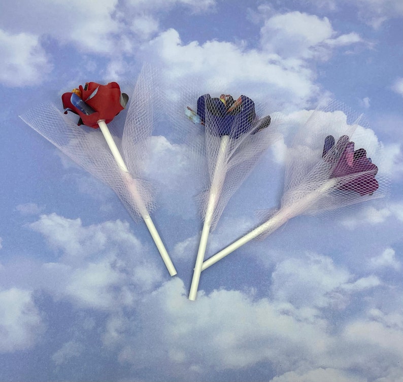 Puede incluir: Tres ramos de flores de papel con tul blanco. Las flores son rojas, moradas y azules.