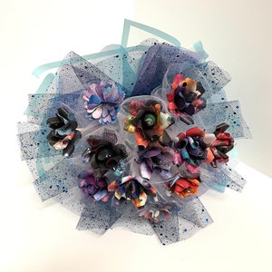 Puede incluir: Un ramo de flores de papel con estampado de galaxia, arreglado en un tul azul con brillantina azul.