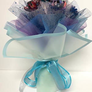 Puede incluir: Un ramo de flores de papel de colores envuelto en tul azul y morado y atado con una cinta azul.