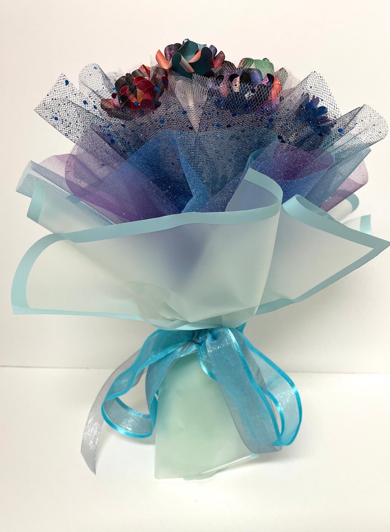 Puede incluir: Un ramo de flores de papel de colores envuelto en tul azul y morado y atado con una cinta azul.