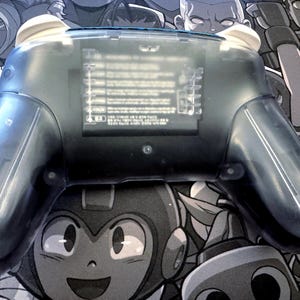 May include: A transparent blue video game controller with white accents. The controller has a clear plastic shell, allowing a view of the internal components. The design includes ergonomic grips and buttons.