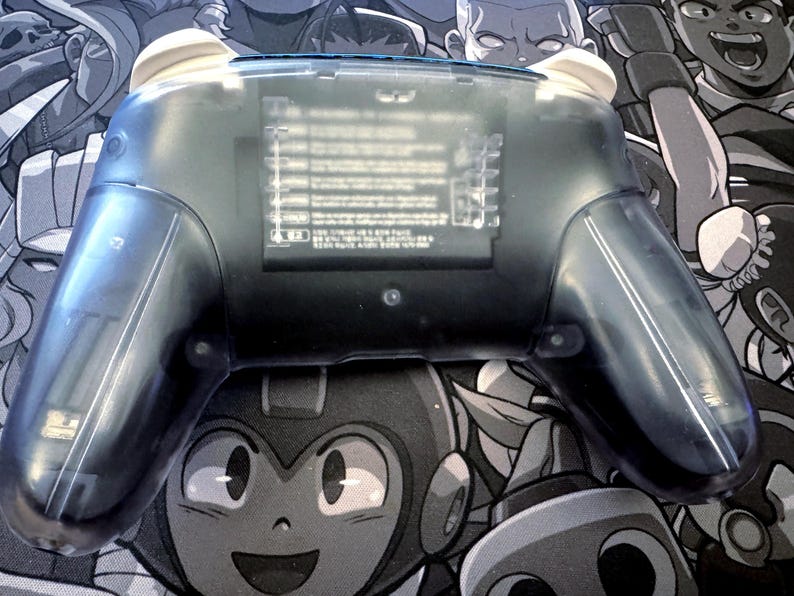 May include: A transparent blue video game controller with white accents. The controller has a clear plastic shell, allowing a view of the internal components. The design includes ergonomic grips and buttons.