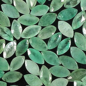 Può includere: Una collezione di pietre preziose di colore verde smeraldo a forma di marquise. Le pietre sono sfaccettate e hanno una finitura liscia e lucida.
