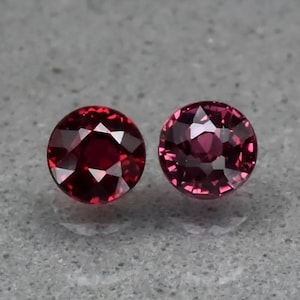 Op de afbeelding: Twee ronde, gefacetteerde, rode edelstenen. De edelstenen zijn gezet in een bezel-setting en hebben een hoge glans.