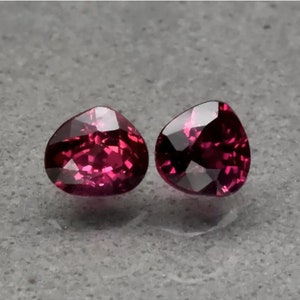 Può includere: Due pietre preziose a forma di cuore, ciascuna con una tonalità rossa profonda e ricca. Le pietre sono sfaccettate e hanno un alto livello di brillantezza. Probabilmente sono rubini o granati.