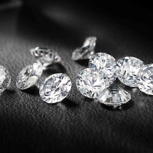 Può includere: Un gruppo di diamanti brillanti e trasparenti sparsi su una superficie nera. I diamanti sono di diverse dimensioni e forme, riflettendo la luce.