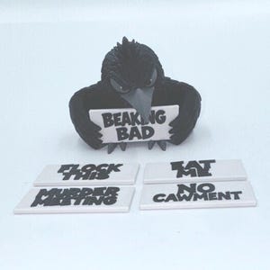 May include: A black crow figurine holding a white rectangular sign that reads BEAKING BAD. Four additional white rectangular signs are included, featuring the black text FLOCK THIS, EAT ME, MURDER MEETING, and NO CAWMENT, all displayed on a white surface.