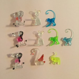 May include: A set of ten clear plastic animal figurines. The animals include a dog, a mouse, a monkey, a swan, and an elephant. The figurines are all different colors, including pink, blue, green, and yellow.