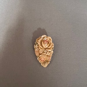 May include: A carved ivory brooch with a cluster of roses and smaller flowers in shades of pink and cream.