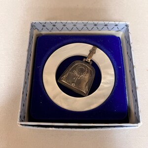 May include: A white teething ring with a silver bell charm attached. The bell has the inscription "First Year" and a design of a wreath with a star in the center.