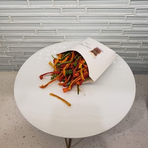 May include: A white paper bag with the text "Raw Bites" printed on it, filled with a colorful mix of dried vegetable strips.