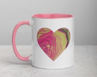 May include: A white ceramic mug with a pink rim and handle. The mug features a pink and yellow abstract heart design.