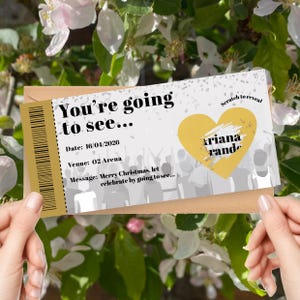 K&ouml;nnte beinhalten: Ein Konzertticket-Design mit dem Text "You're going to see..." und "ariana rande" in einem gelben Herzen. Das Ticket enth&auml;lt das Datum 16.04.2026 und den Veranstaltungsort "O2 Arena". Die Nachricht lautet "Merry Christmas, let celebrate by going to see..."