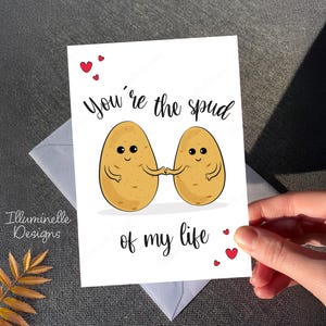 May include: A white card with a cute illustration of two potatoes holding hands. The card says "You're the spud of my life" with red hearts.