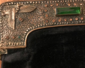 May include: A black velvet evening bag with a gold metal clasp. The clasp features a bird design with green and gold accents.