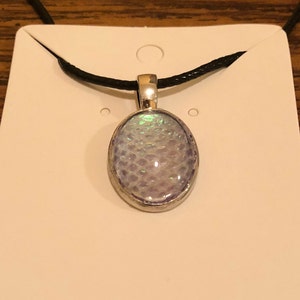 May include: A silver oval pendant necklace with a iridescent, light blue, textured glass insert. The necklace is on a black cord.