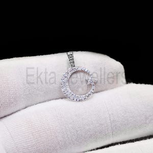 May include: A silver pendant in the shape of a crescent moon and star, encrusted with small, clear gemstones. The pendant is on a white surface, with the text "Ekta Jewellers" partially visible.