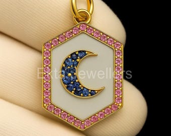 Könnte beinhalten: Goldfarbener Anhänger mit sechseckiger Form aus weißem Emaille, mit einem Mond-Design aus blauen Edelsteinen. Der Anhänger ist mit rosa Edelsteinen umrandet und trägt den Text "Exte Jewellers".