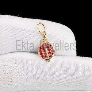 May include: A gold-colored pendant in the shape of a pomegranate, encrusted with small red gemstones. The pendant has a loop at the top for a chain. The text "Ekta sellers" is visible on the background.