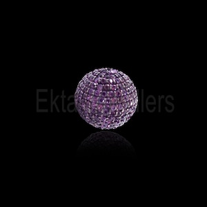 Könnte beinhalten: Eine kugelförmige Perle, bedeckt mit kleinen, runden, lila Edelsteinen. Die Perle ist vor einem schwarzen Hintergrund platziert, mit einer subtilen Reflexion darunter. Der Gesamteindruck ist luxuriös und detailliert.