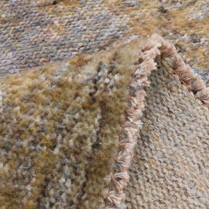 以下が含まれることがあります： フリンジが付いた織り絨毯の端のクローズアップ。絨毯は茶色、ベージュ、グレーの色が混ざっています。