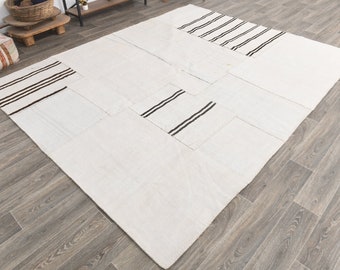 Può includere: Un tappeto bianco a patchwork con strisce nere. Il tappeto è composto da diversi pezzi di tessuto cuciti insieme. Il tappeto è su un pavimento di legno.