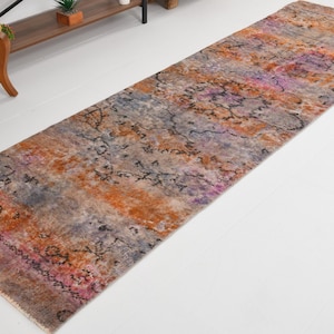 May include: A long rectangular runner rug featuring a distressed, multi-colored pattern in shades of burnt orange, muted purple, grey, and black. The rug displays a faded, intricate floral and medallion design across its entire surface area.