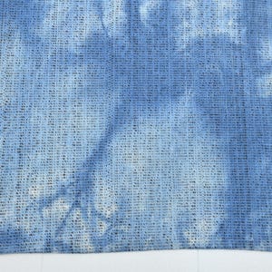 Pu&ograve; includere: Un primo piano di un tessuto tie-dye blu e bianco con una trama tessuta.