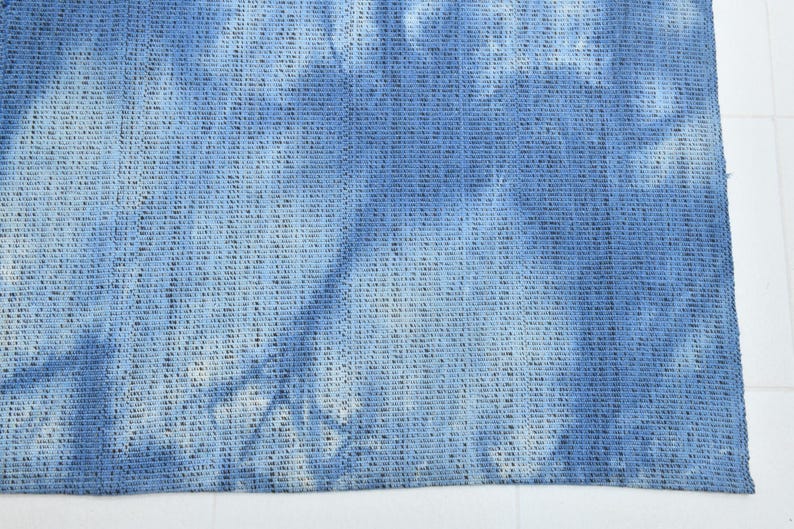 Pu&ograve; includere: Un primo piano di un tessuto tie-dye blu e bianco con una trama tessuta.