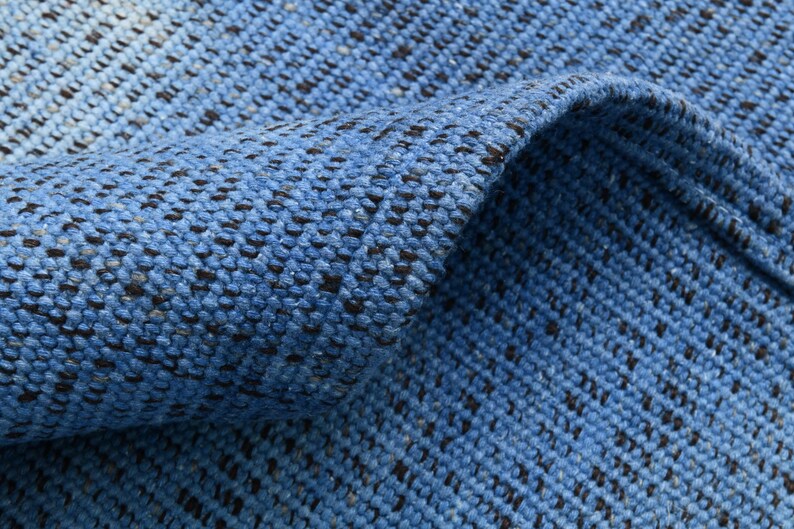 Pu&ograve; includere: Primo piano di un tappeto tessuto blu e nero con una superficie testurizzata. Il tappeto &egrave; realizzato in un materiale morbido e resistente e presenta un effetto sfumato sottile.