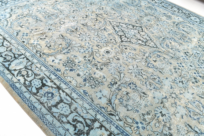 May include: A vintage rug with a blue and white floral pattern. The rug has a faded look and a dark blue border.
