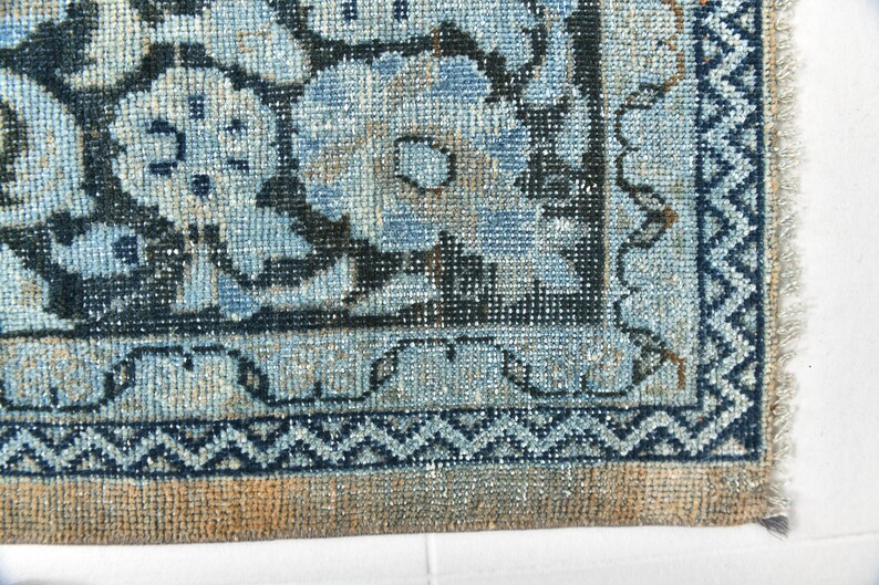 May include: Close-up of the bottom edge of a blue and beige rug with a geometric pattern. The rug has a fringe border.