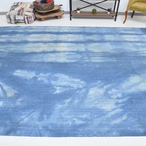 Pu&ograve; includere: Un tappeto blu e bianco tie-dye con un sottile motivo a righe. Il tappeto ha un aspetto sbiadito e vintage.