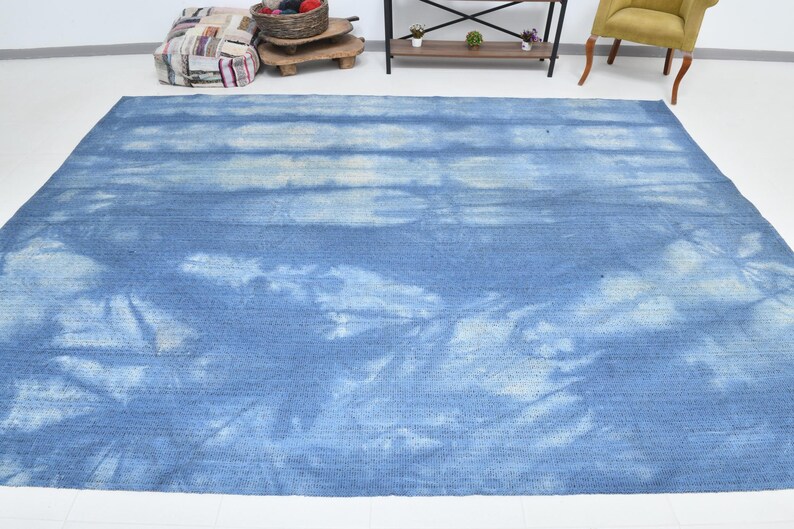 Pu&ograve; includere: Un tappeto blu e bianco tie-dye con un sottile motivo a righe. Il tappeto ha un aspetto sbiadito e vintage.