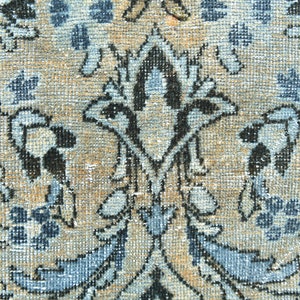 May include: Close-up of a beige rug with a blue and black floral pattern. The rug has a woven texture and a distressed look.