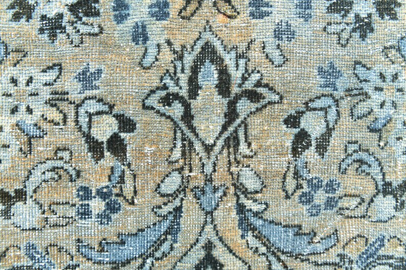 May include: Close-up of a beige rug with a blue and black floral pattern. The rug has a woven texture and a distressed look.
