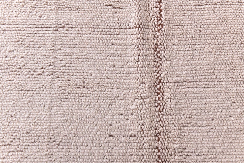 Pu&ograve; includere: Primo piano di un tappeto beige chiaro strutturato. Il tappeto ha un aspetto tessuto con una striscia verticale di beige pi&ugrave; scuro, creando un contrasto sottile. La superficie &egrave; dettagliata con piccoli anelli in rilievo.
