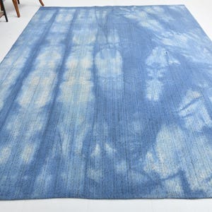 Pu&ograve; includere: Un tappeto blu e bianco tie-dye con una texture sottile. Il tappeto ha un aspetto sbiadito e vintage.