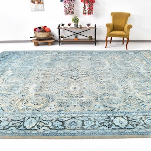 May include: A vintage blue and cream rug with a floral pattern and a dark blue border. The rug is laid out on a white floor.