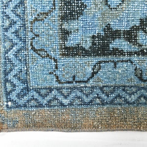 May include: Close-up of the bottom edge of a blue and black patterned rug with a fringe border. The rug has a faded, vintage look.
