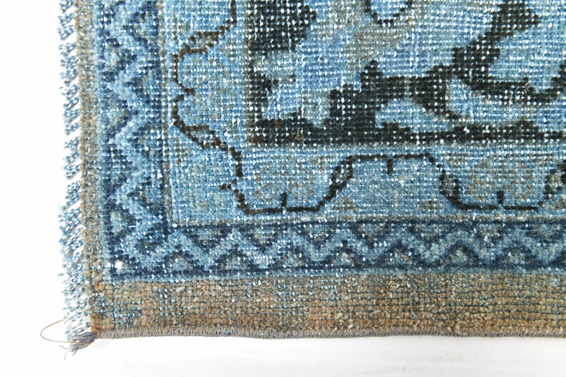 May include: Close-up of the bottom edge of a blue and black patterned rug with a fringe border. The rug has a faded, vintage look.