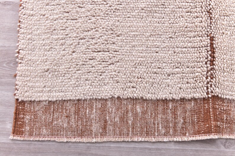 Pu&ograve; includere: Primo piano di un tappeto beige e marrone strutturato. La sezione superiore &egrave; beige chiaro con una trama nodosa, mentre la sezione inferiore &egrave; marrone scuro con un motivo intrecciato. Una striscia marrone verticale corre lungo il lato destro.