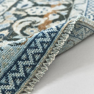 May include: Close-up of a blue and white patterned rug with fringed edges. The rug is folded in half, showing the intricate details of the woven design.