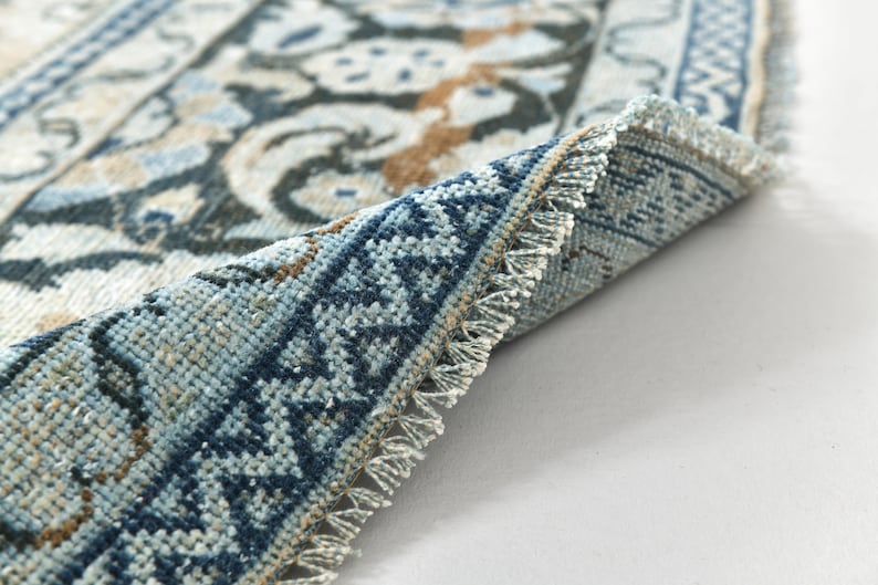May include: Close-up of a blue and white patterned rug with fringed edges. The rug is folded in half, showing the intricate details of the woven design.